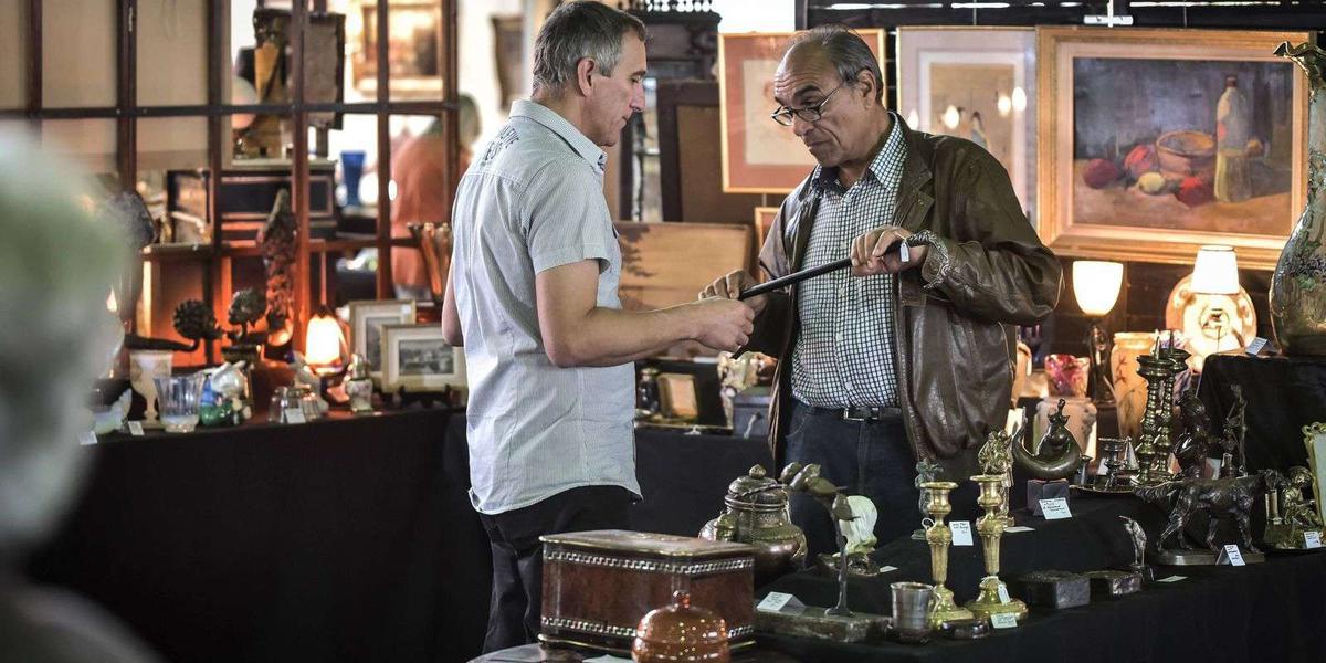 Deux hommes examinent des antiquités dans un marché aux puces animé.
